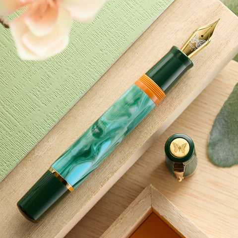 Delta butterfly fountain pen with green body and gold butterfly nib resting on a wooden desk.
