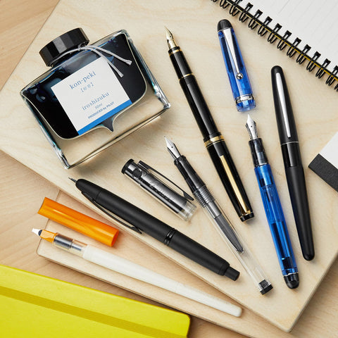 Iroshizuku Konpeki ink bottle beside a black fountain pen on a light wood desk with a spiral notebook