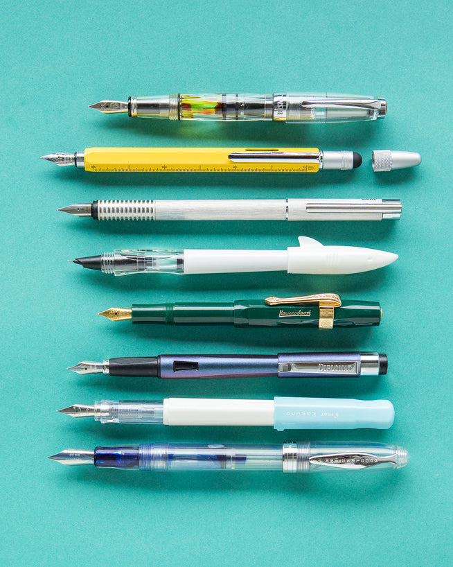 8 fountain pens lined up, all uncapped on turquoise background
