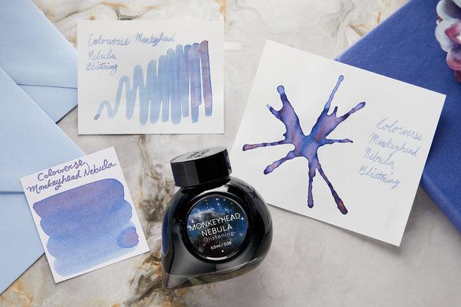 Colorverse Monkeyhead Nebula Glistening fountain pen ink bottle, writing sample, swab and swatch on white background with purple envelopes