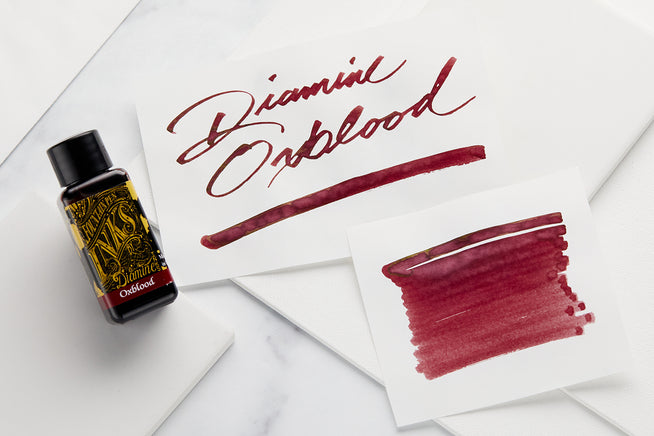 Diamine Oxblood fountain pen ink 30 mL bottle with 3 white cards that have swatch, and writing of name on them, respectively