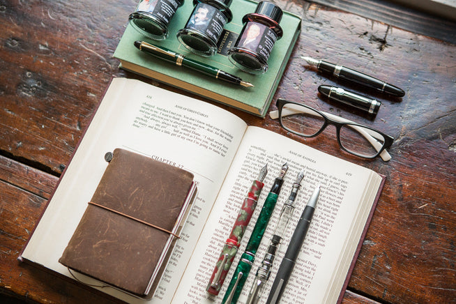 Assorted fountain pens uncapped on a book with ink 