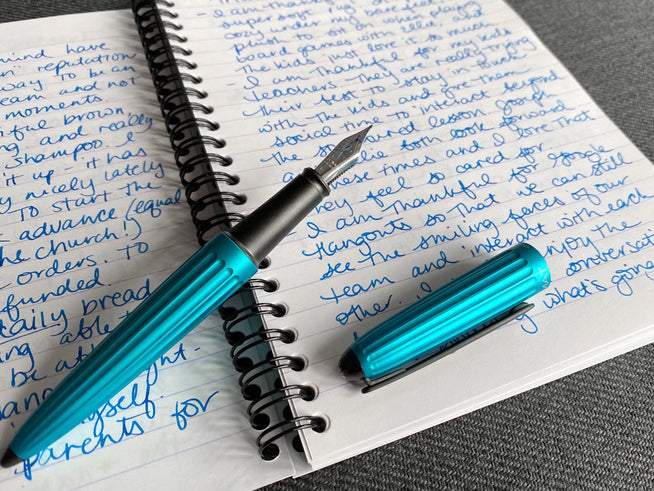 A teal fountain pen on top of a wirebound notebook filled with writing
