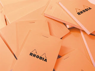 Rhodia orange notebooks in a pile on a desk