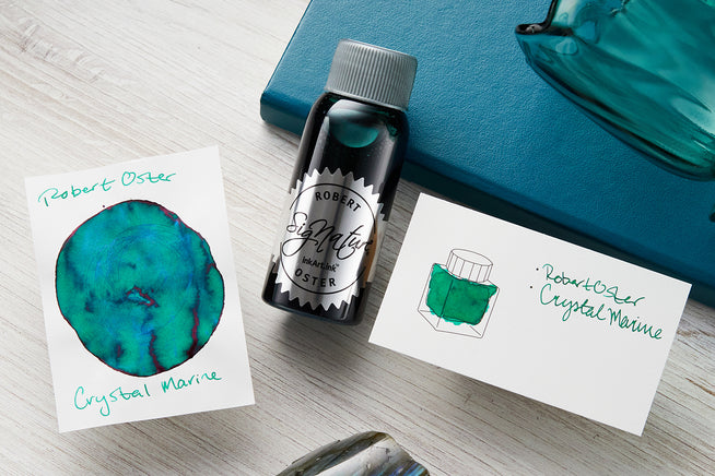 Robert Oster Fountain Pen ink bottle with 2 ink swab cards with a teal journal in the background