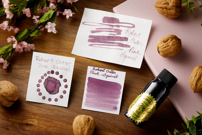 Robert Oster Pink Squirrel fountain pen ink, bottle, and color swabs on wooden desk background