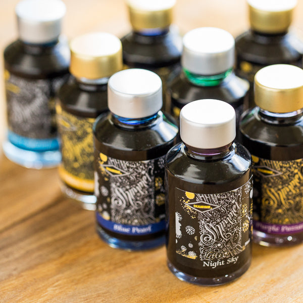 Eight closed bottles of fountain pen ink on a wooden surface.