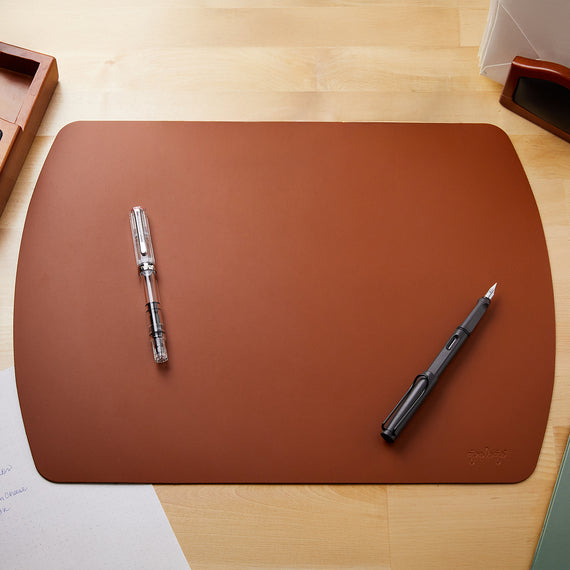 Cognac-colored writing mat, rectangular in shape with rounded sides and corners. Suitable for desk use.