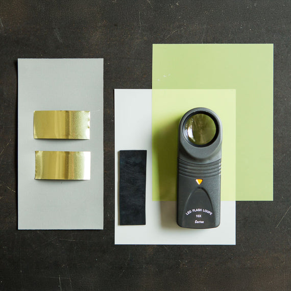 Black handheld light source on a white card with gold and black samples on gray and green cards.