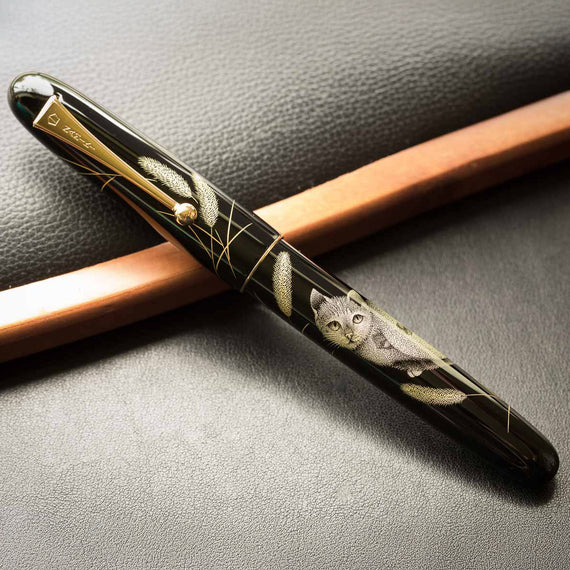 Black fountain pen with engraved gold cat on a black textured background