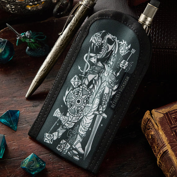 Black pouch with white design on a wooden surface with dice and a book
