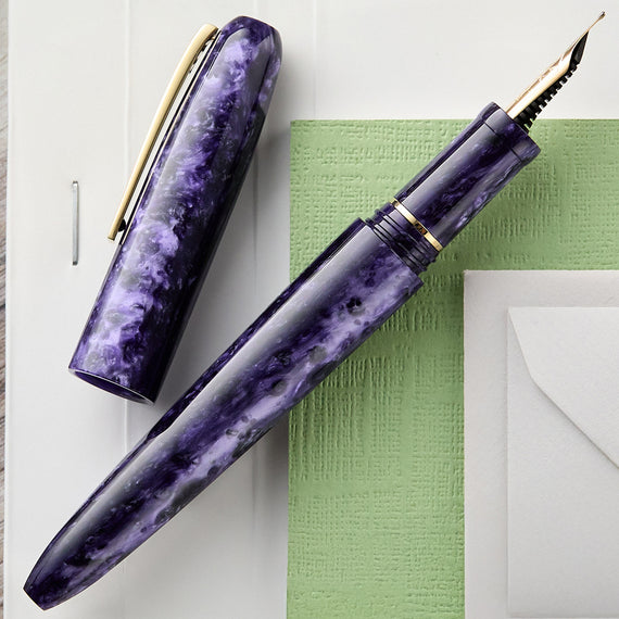 Purple marbleized fountain pen on a white surface with a green paper and envelope.